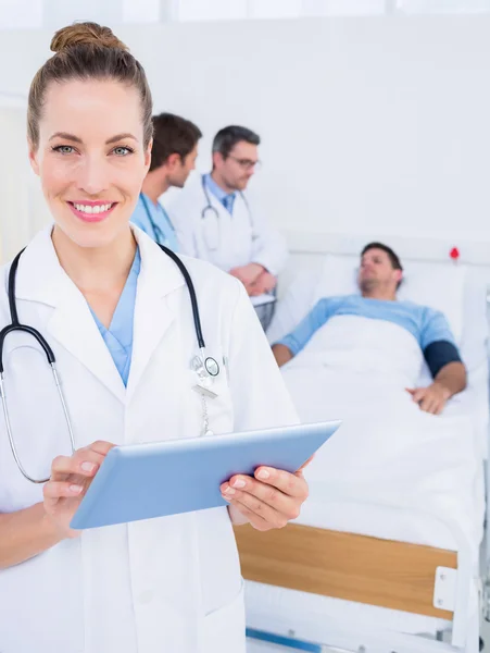 Doctor using digital tablet with colleagues and patient behind — Stock Photo, Image