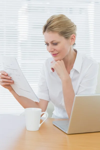 Donna d'affari che legge un documento oltre al computer portatile alla scrivania — Foto Stock