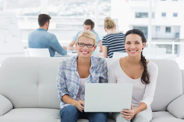 Las mujeres que utilizan el ordenador portátil con sus colegas en segundo plano en creativo off — Foto de Stock