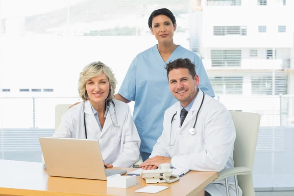 Medici sorridenti con computer portatile a studio medico — Foto Stock