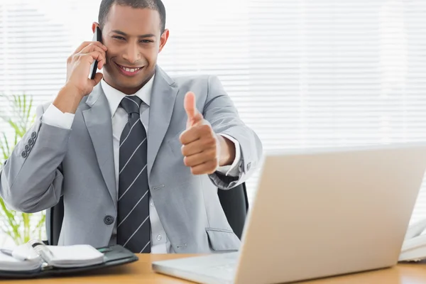 Businessman gesturing thumbs up while on call at office desk — Stock Photo, Image