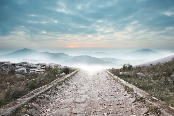 Stony path leading to misty mountain range — Stock Photo, Image