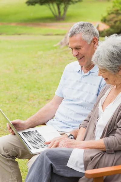 Lachende senior koppel met behulp van laptop in het park — Stockfoto