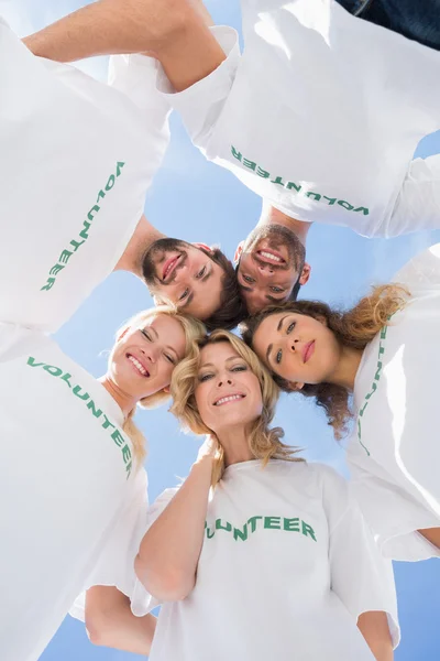 Gelukkig vrijwilligers vormen een huddle tegen blauwe hemel — Stockfoto