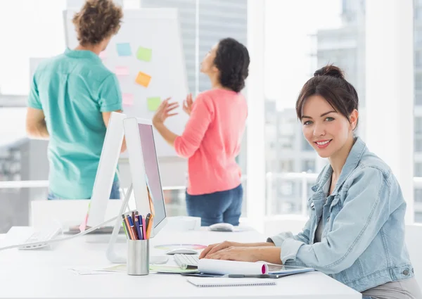 Casual woman using computer with colleagues behind in office — Stock Photo, Image