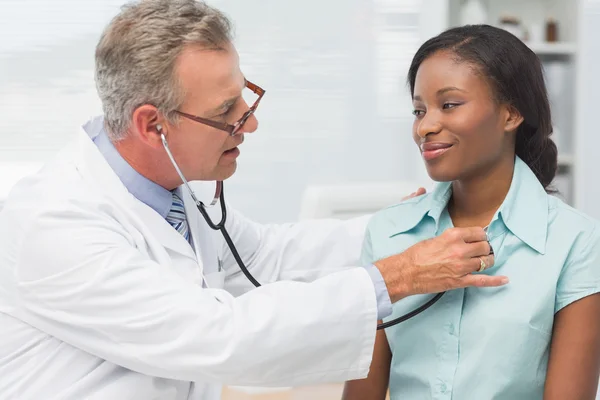Médico ouvindo alegres pacientes jovens peito com estetosco — Fotografia de Stock