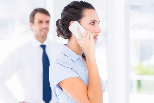 Woman on call with male colleague in background — Stock Photo, Image