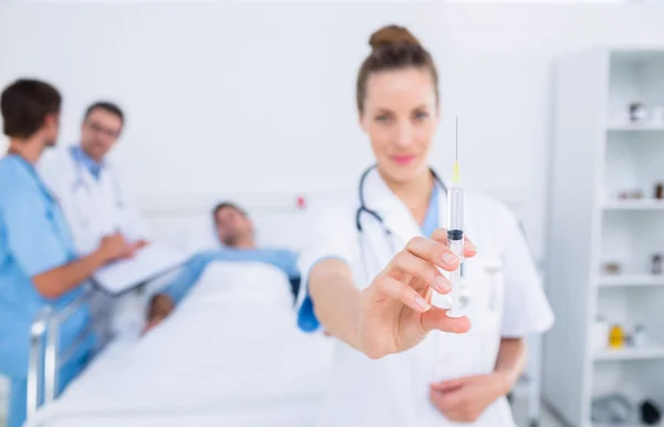 Médico segurando seringa com colegas e paciente no hospital — Fotografia de Stock