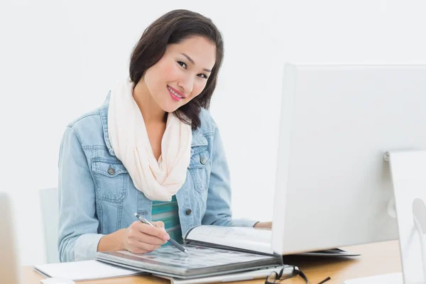 Sorrindo mulher casual com catálogo na frente do computador no escritório — Fotografia de Stock