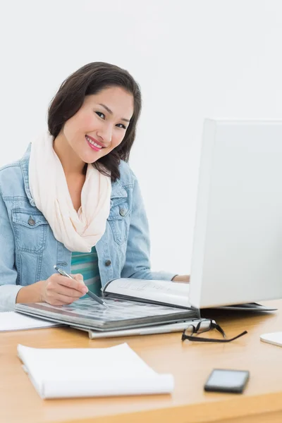 Sorrindo mulher casual com catálogo na frente do computador no escritório — Fotografia de Stock