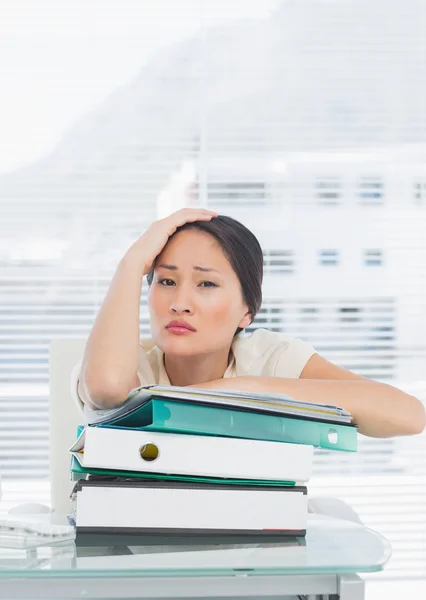 Gelangweilte Geschäftsfrau mit einem Stapel Ordner am Schreibtisch — Stockfoto