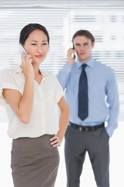 Empresaria y hombre usando teléfonos celulares en la oficina — Foto de Stock