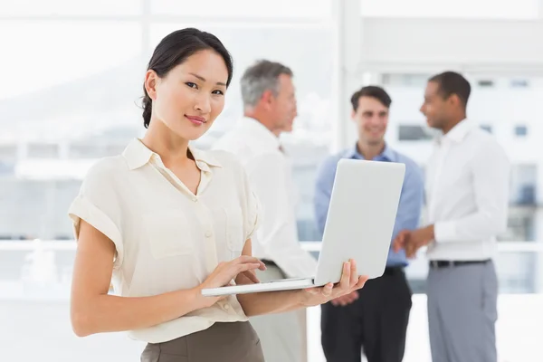 Asiática mujer de negocios utilizando ordenador portátil con equipo detrás de su — Foto de Stock