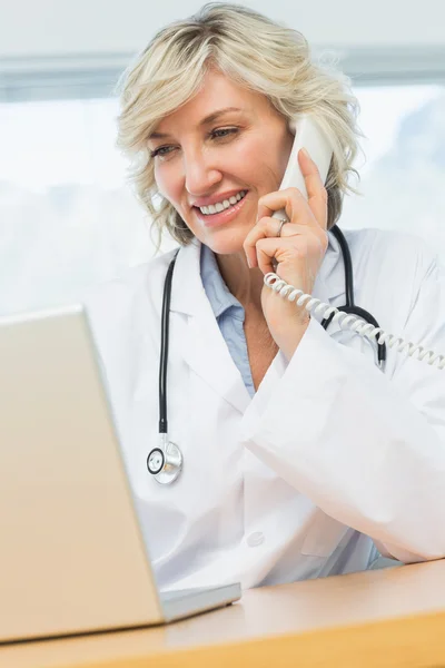一位女医生在医疗办公室使用笔记本电脑和手机 — 图库照片
