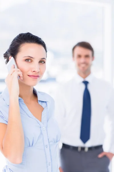 Woman on call with male colleague in background — Stock Photo, Image