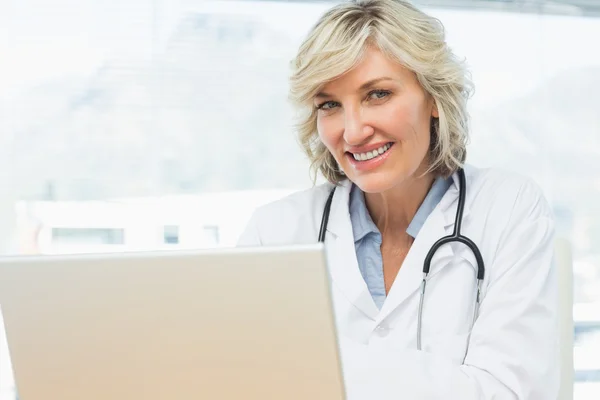 Médica sorridente usando laptop em consultório médico — Fotografia de Stock