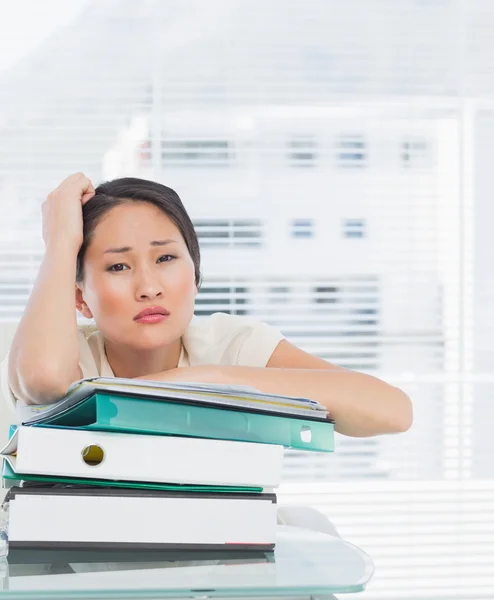 Gelangweilte Geschäftsfrau mit einem Stapel Ordner am Schreibtisch — Stockfoto