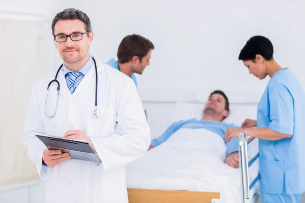 Doctor holding reports with patient and surgeon in background — Stock Photo, Image