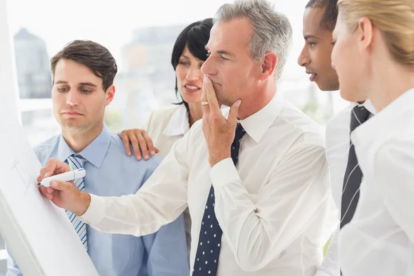 Kollegen beobachten denkenden Geschäftsmann beim Schreiben auf Whiteboard — Stockfoto