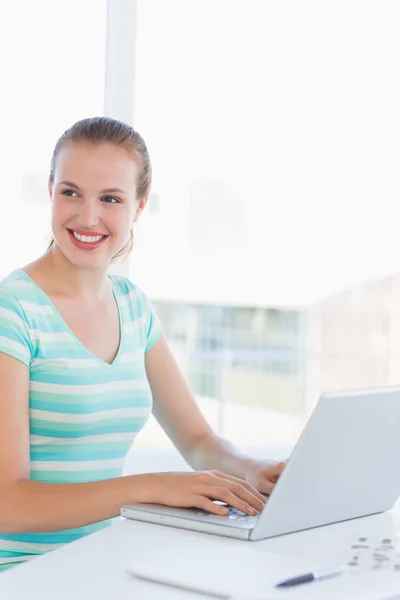 Jovem mulher casual usando laptop em um escritório brilhante — Fotografia de Stock