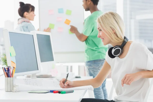 Artist drawing something on paper with colleagues behind at offi — Stock Photo, Image