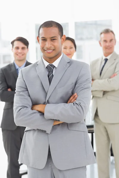 Empresario sonriendo a la cámara con el equipo detrás de él — Foto de Stock