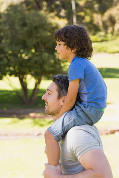 Улыбающийся мужчина носит сына на плечах в парке — стоковое фото
