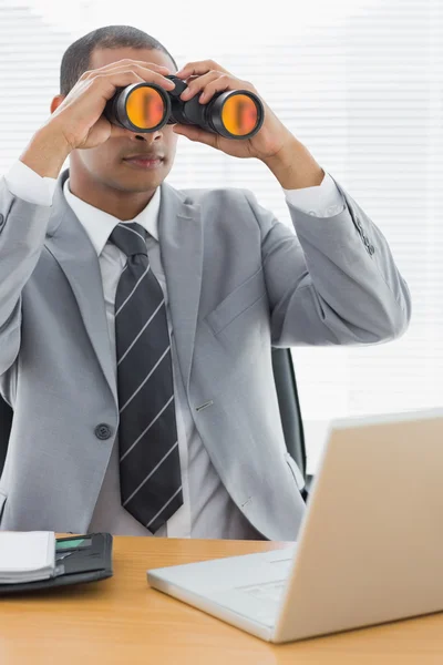 Businessman with binoculars in front of laptop at office — Stock Photo, Image