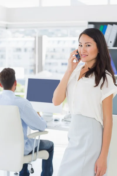 Female artist using mobile phone with colleague in background — Stock Photo, Image