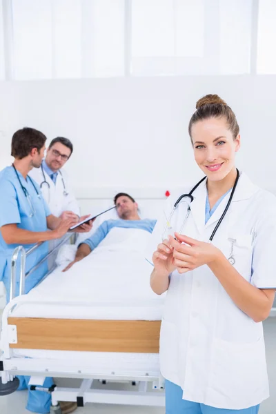 Doctor holding syringe with colleagues and patient in hospital — Stock Photo, Image