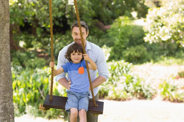 Felice padre spingendo ragazzo su swing — Foto Stock