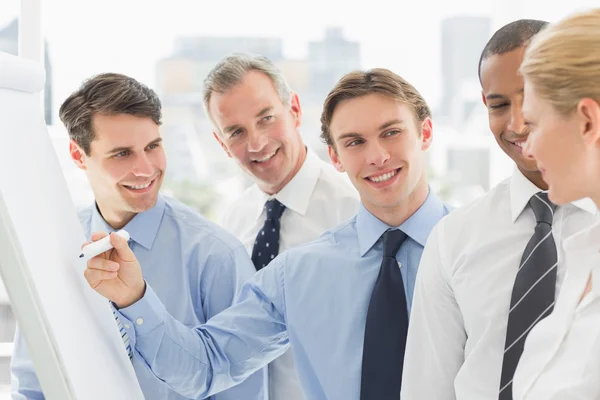 Jonge zakenman schrijven op whiteboard met collega 's — Stockfoto