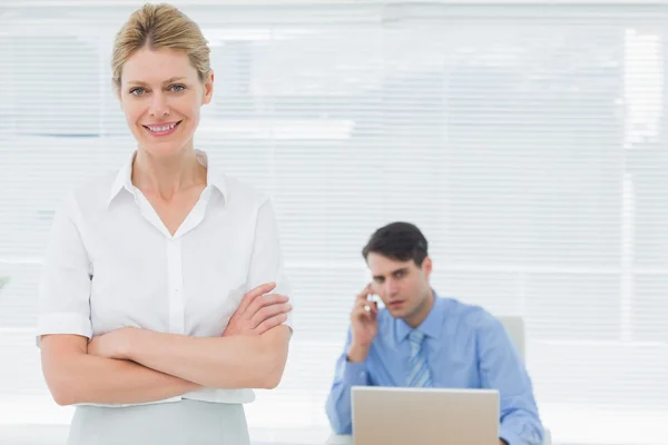 Smiling businesswoman with man working behind at office — Stock Photo, Image