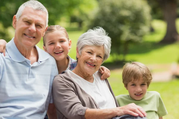 Smiling senior couple and grandchildren at park — Stock Photo, Image