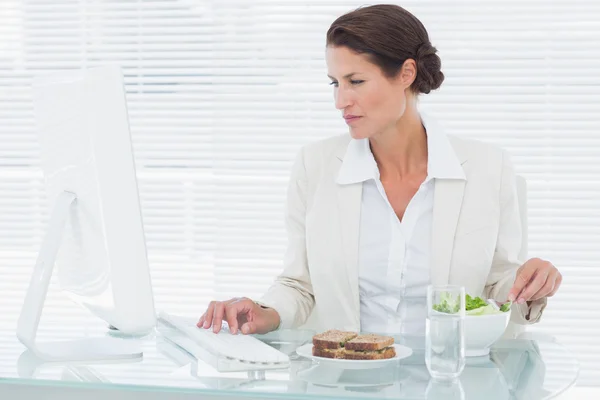 Affärskvinna med datorn samtidigt äta sallad på skrivbord — Stockfoto