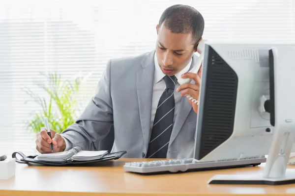 Uomo d'affari che utilizza computer e telefono alla scrivania dell'ufficio — Foto Stock