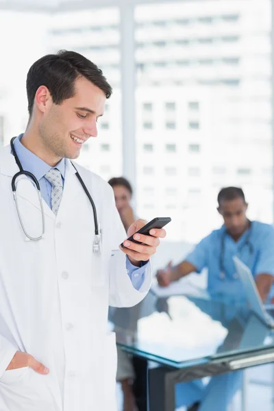 Doctor text messaging with group around table in hospital — Stock Photo, Image