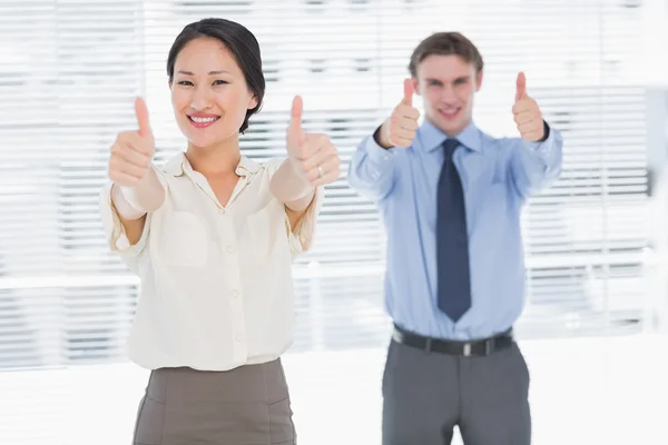 Business colleagues gesturing thumbs up in office — Stock Photo, Image