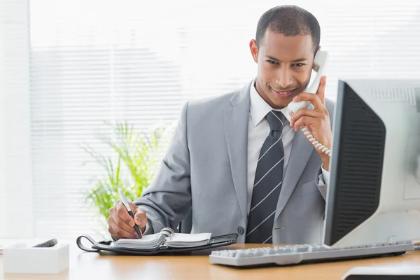 Lachende zakenman met behulp van computer en telefoon op kantoor — Stockfoto