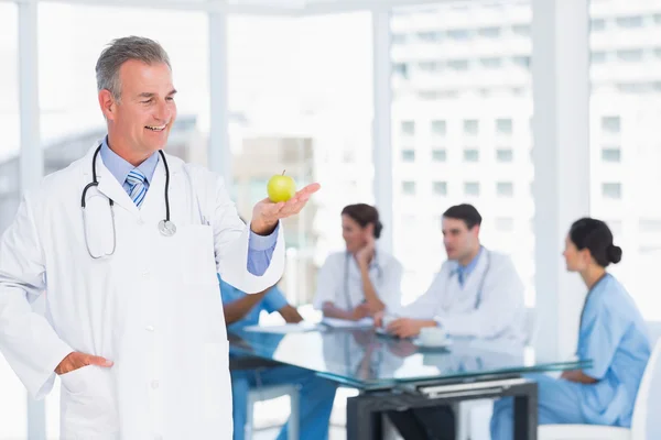 Médico sosteniendo manzana con grupo alrededor de la mesa en el hospital —  Fotos de Stock