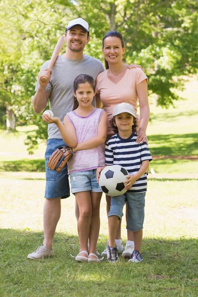 Family of four holding baseball bat and ball in park — Stock Photo, Image