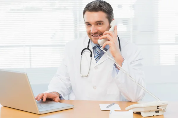 Médico masculino usando laptop y teléfono en consultorio médico —  Fotos de Stock