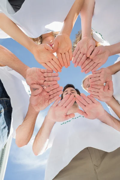 Voluntários felizes com as mãos juntas contra o céu azul Imagem De Stock