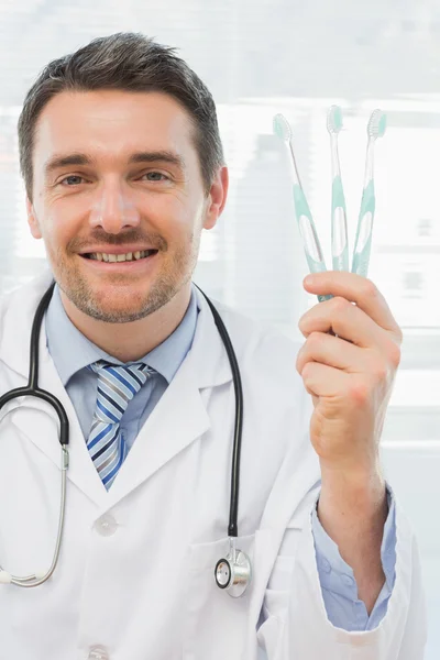 Médico sonriente sosteniendo cepillos de dientes en el consultorio —  Fotos de Stock