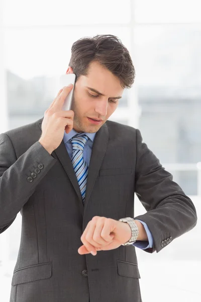 Uomo d'affari serio che controlla l'ora mentre al telefono — Foto Stock