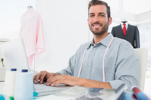 Sonriente diseñador de moda masculino usando el ordenador portátil en el estudio —  Fotos de Stock