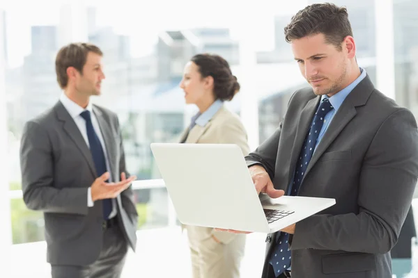 Businessman using laptop with colleagues discussing in office — Stock Photo, Image