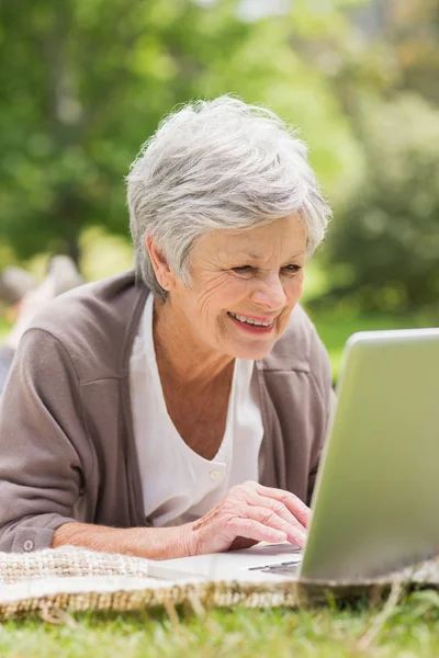 Femme âgée souriante utilisant un ordinateur portable au parc — Photo