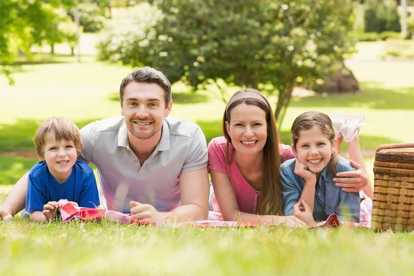 Smiling couple with young kids lying in park — Stock Photo, Image