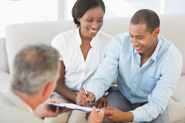 Young smiling couple signing contract on the couch — Stock Photo, Image